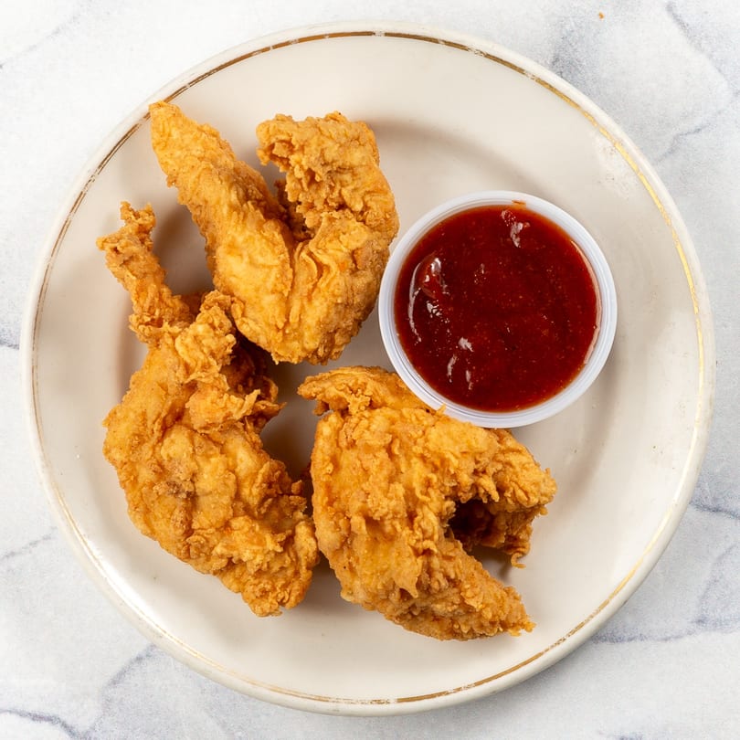 Crispy fried chicken tenders with a side of dark red dipping sauce on a white plate.