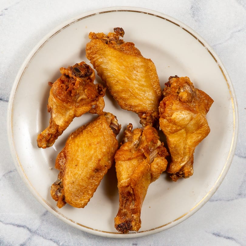 Five crispy, golden-brown fried chicken wings are arranged on a white plate with a gold rim.