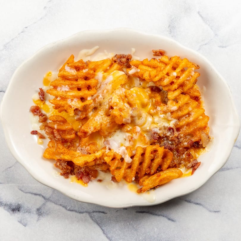 Waffle fries covered in melted cheese and ground meat, served in a white bowl.