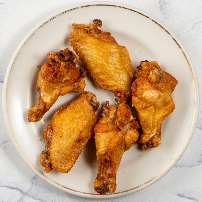 Five golden-brown, crispy fried chicken wings arranged on a white plate with a gold rim.