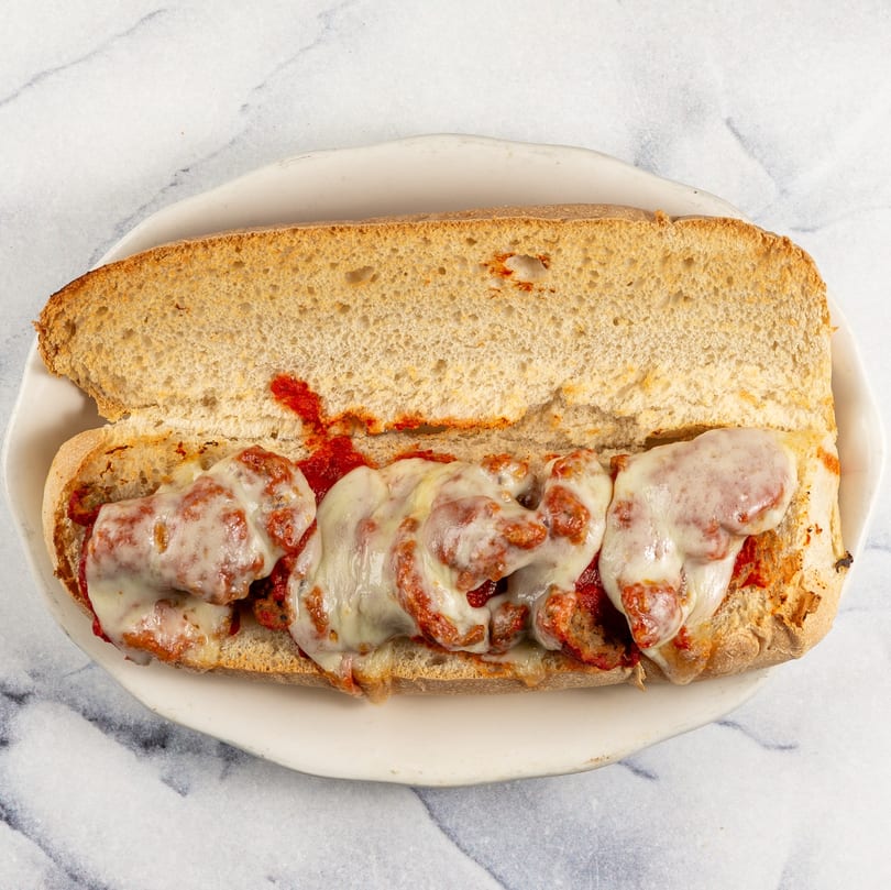 Mike N' Dangelo's meatball sub with melted mozzarella cheese and marinara sauce on a white plate.